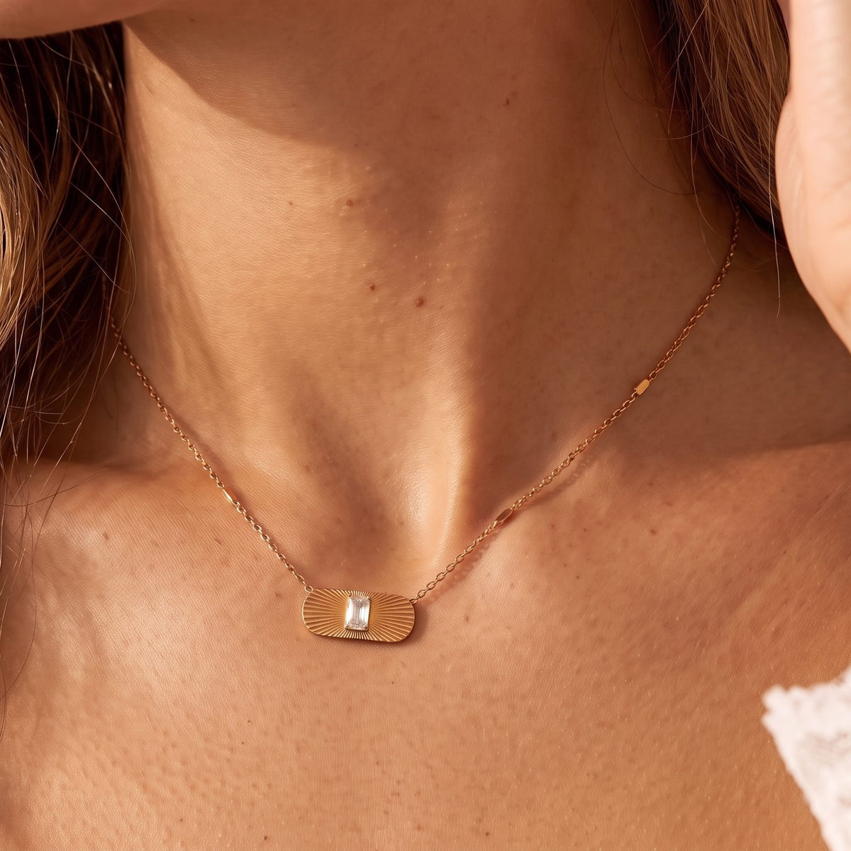 Close-up of the Sunburst Tag Necklace at the collarbone, highlighting its center crystal under warm light, in rose gold