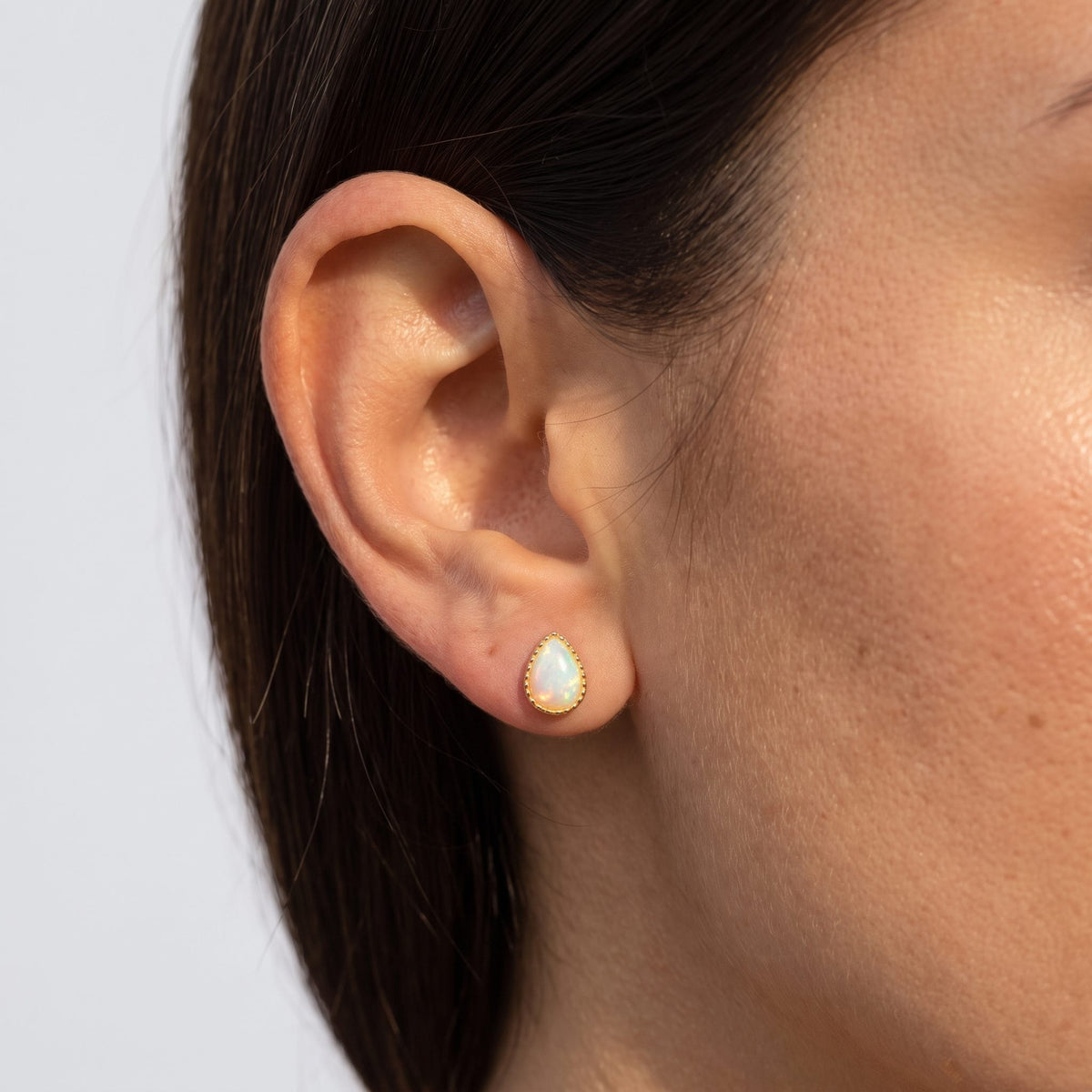 Woman wearing the Teadora Opal Teardrop Earrings on the lobe with a gold-colored frame