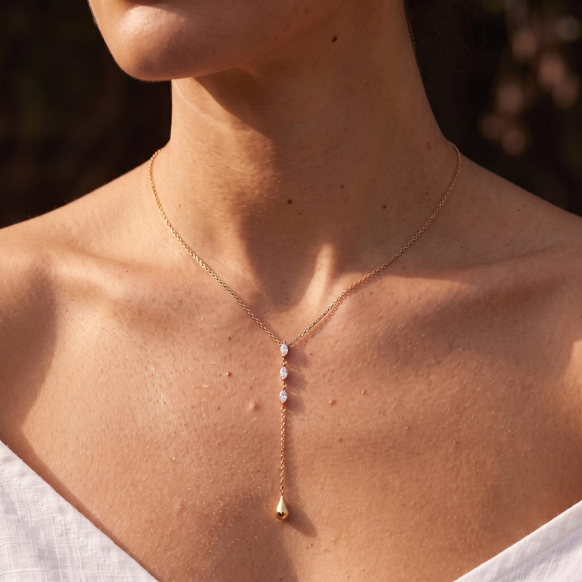 Woman wearing the Teardrop Lariat Necklace at the collarbone in warm sunlight, in rose gold