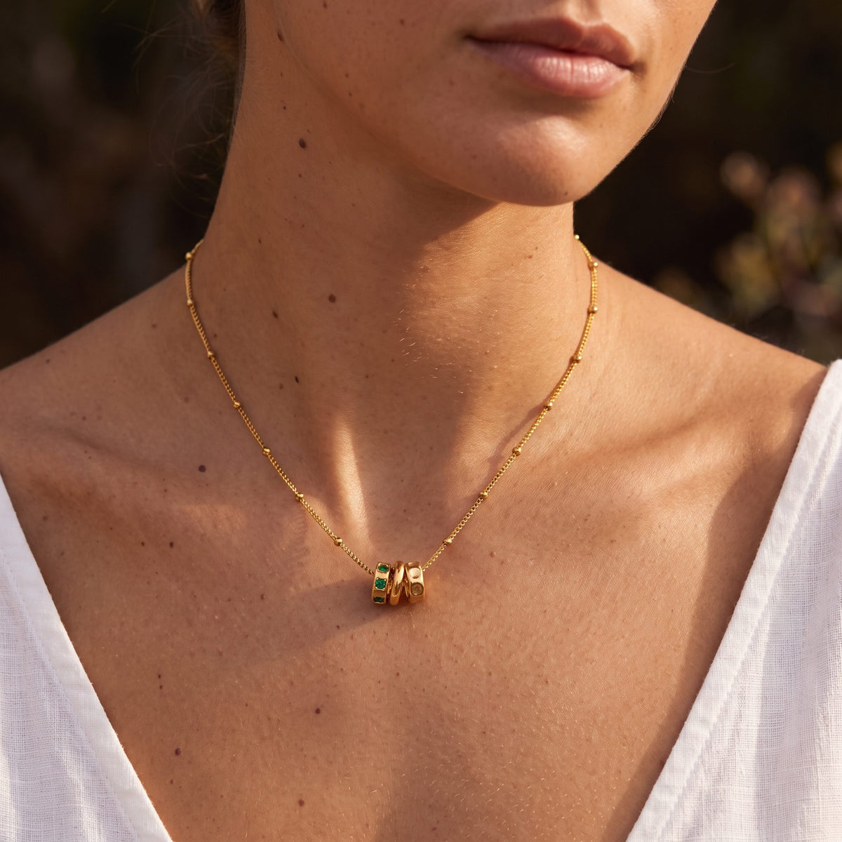 Woman wearing the Three Ring Necklace at her collarbone in warm sunlight with a white top
