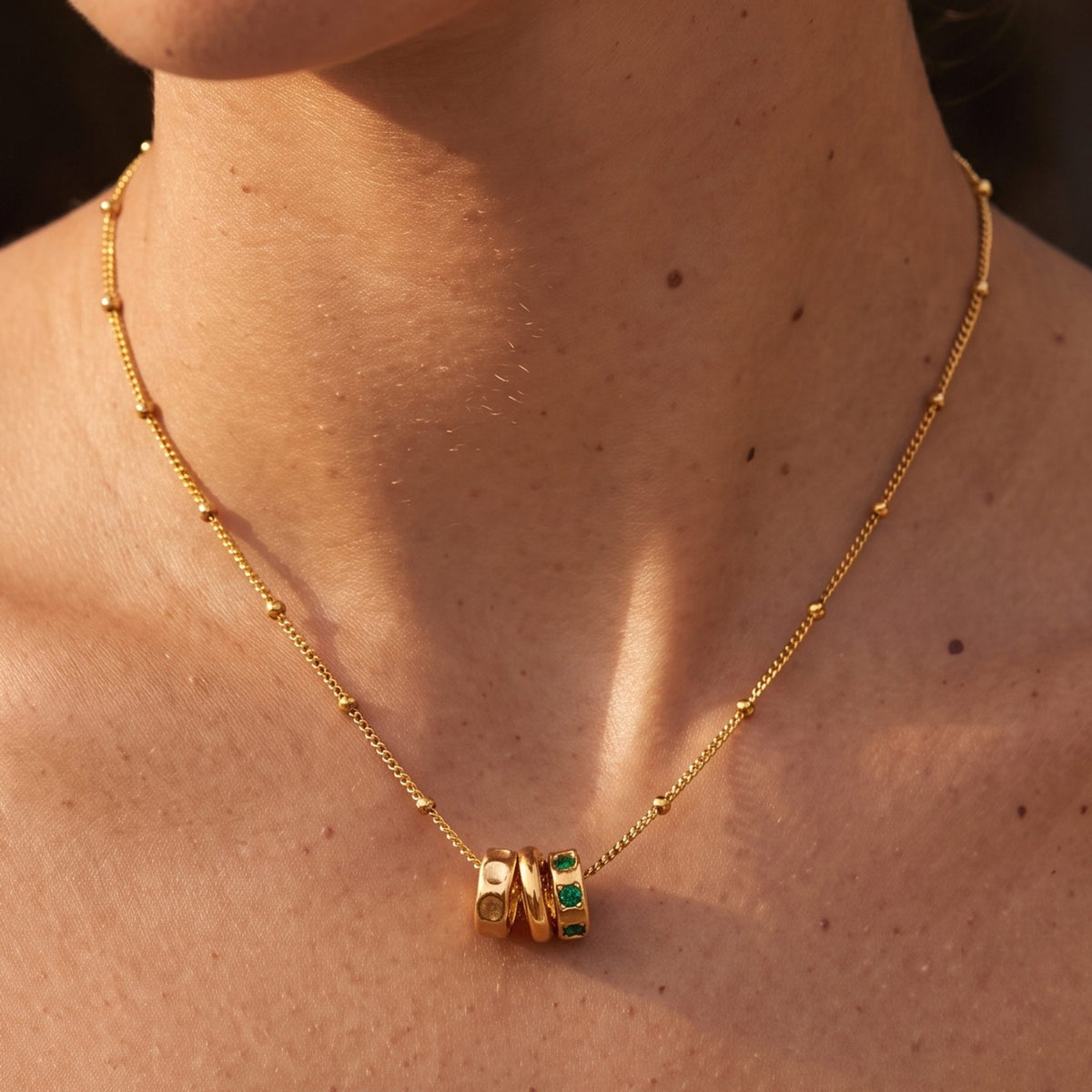 Close-up of the Three Ring Necklace at the collarbone showing green crystals in one ring