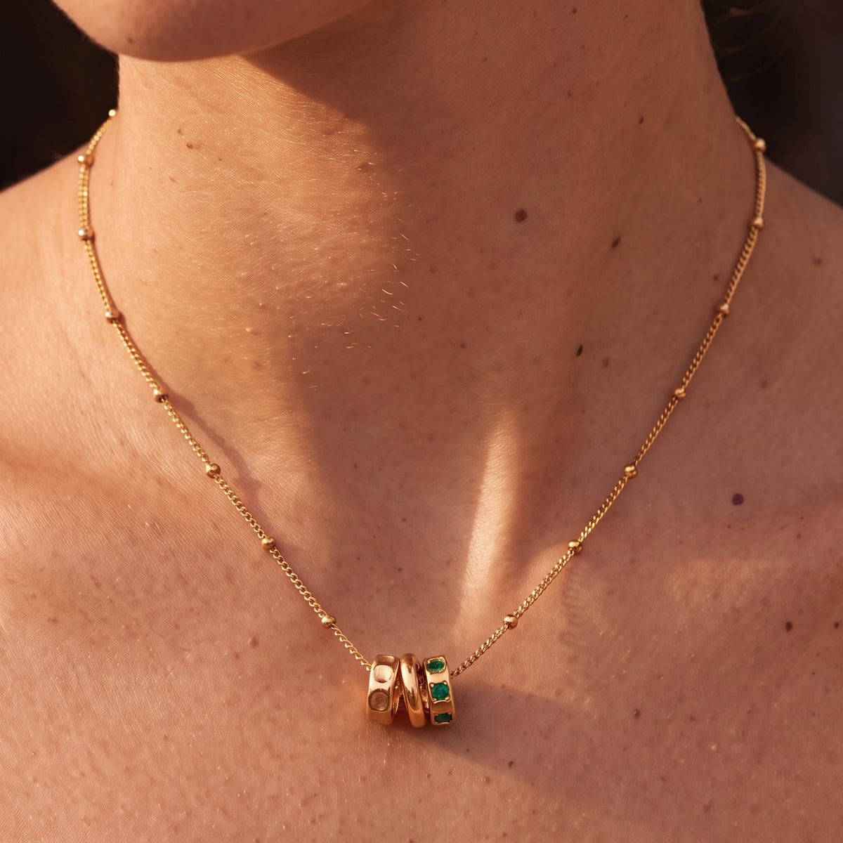 Close-up of the Three Ring Necklace at the collarbone showing green crystals in one ring, in rose gold