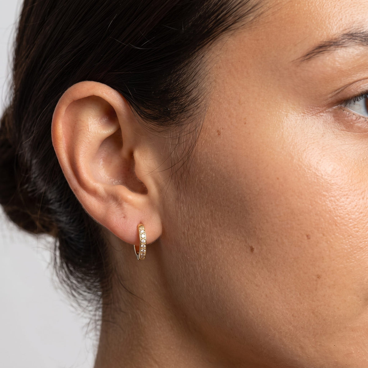Woman wearing the Tina Hoop Earrings through the lobe, featuring a small gold-colored hoop with tiny crystals