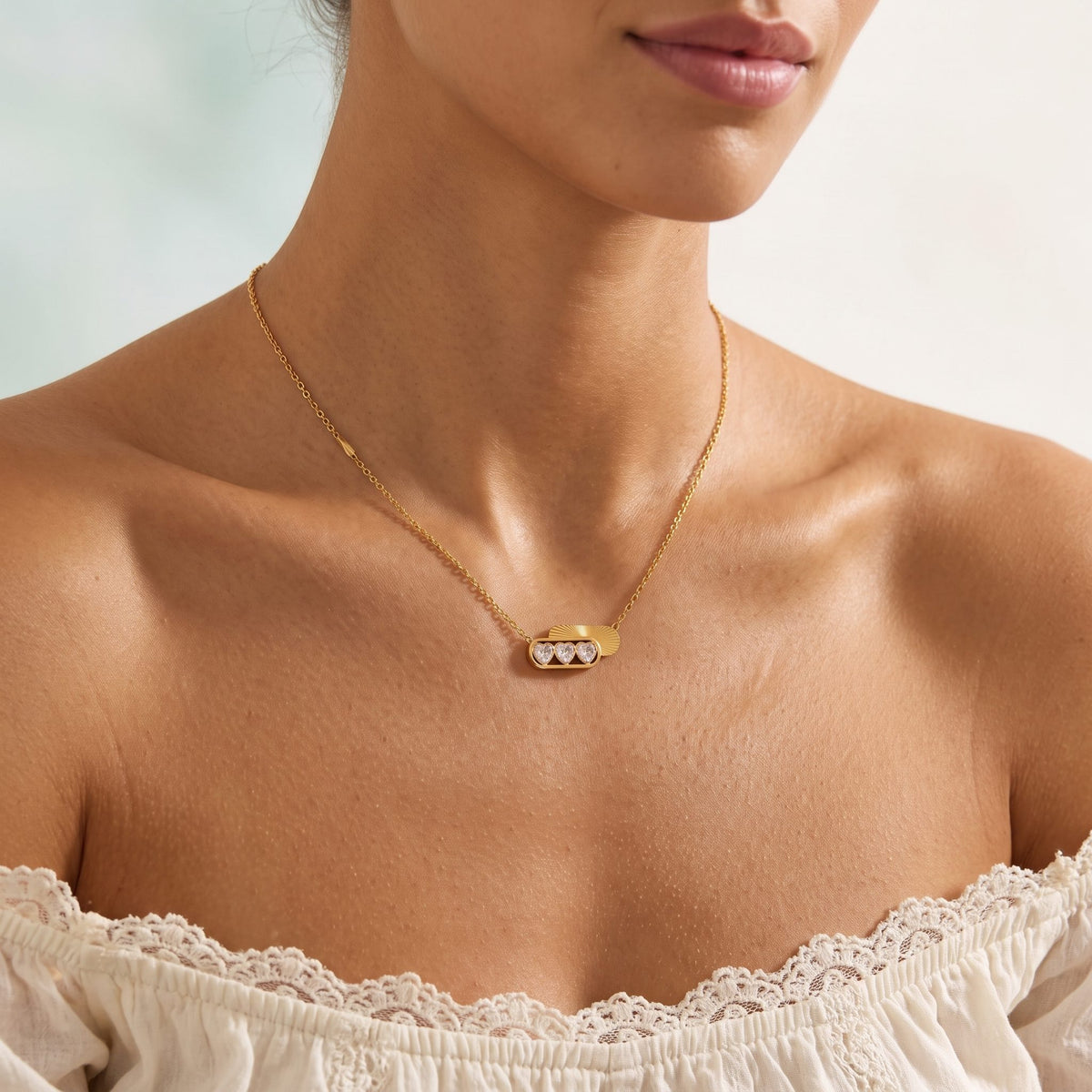 Woman wearing the Triple Heart Necklace at the collarbone in a white lace off-the-shoulder top