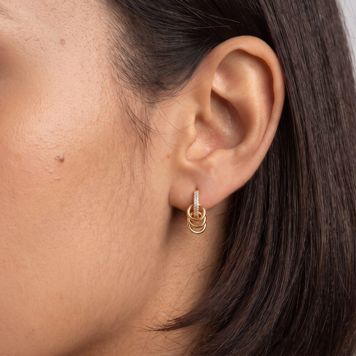 Woman wearing the Triple Loop Huggies on her earlobe, with her dark hair tucked behind her ear