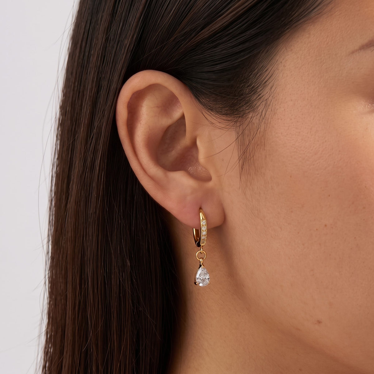 Woman wearing the Vittoria Crystal Water Drop Gold Earrings hanging below the lobe with a teardrop charm