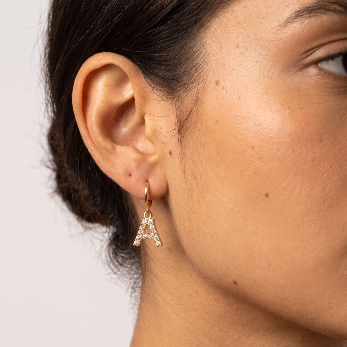 Woman wearing the Wilhemina Initial Letter Earrings featuring a crystal letter A charm hanging below the lobe