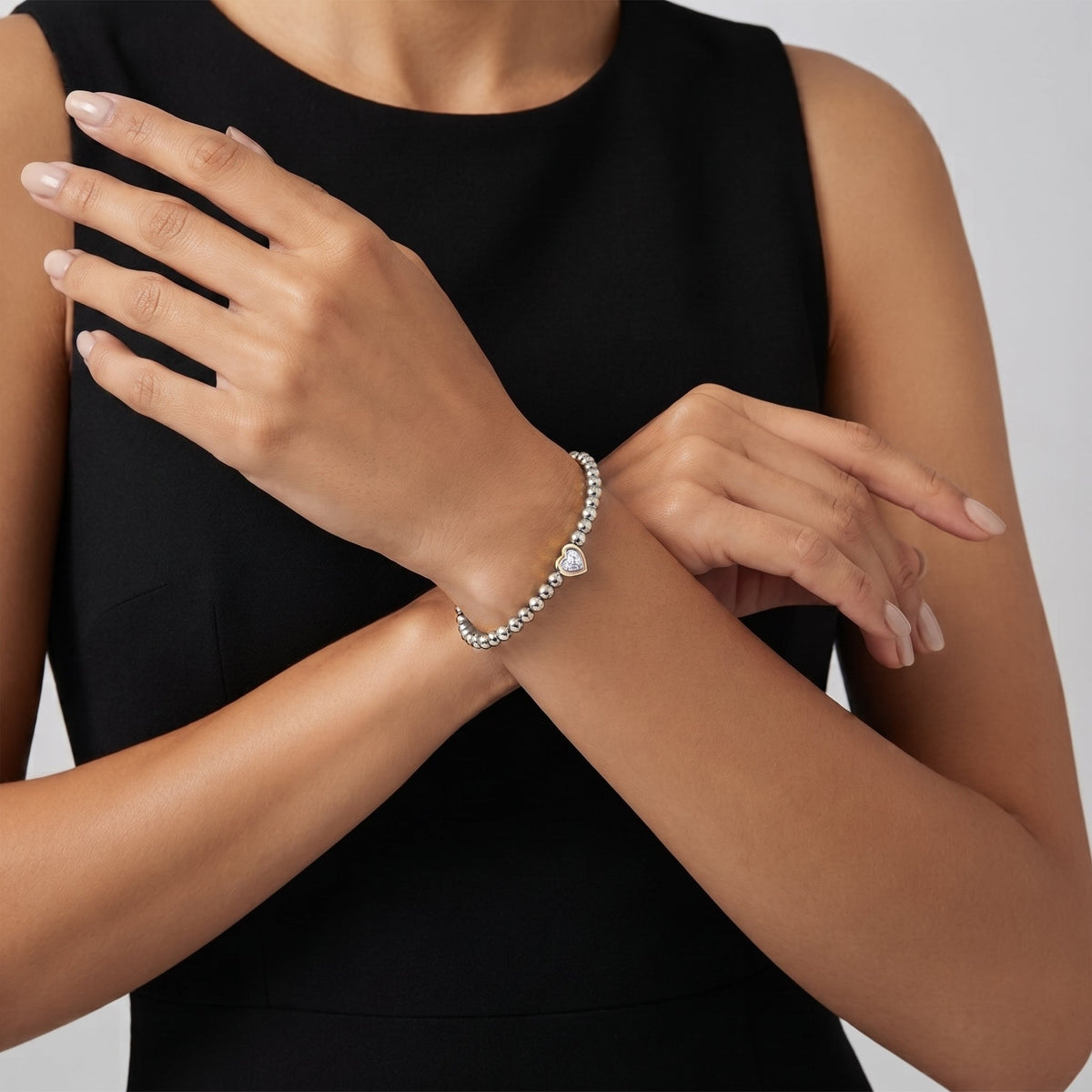 Aurélie heart beaded silver bracelet worn with a black dress, arms crossed at the wrist