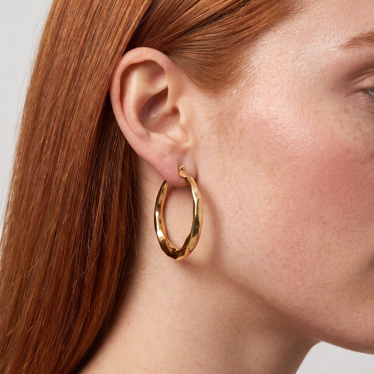 Woman wearing the Aira Hoop Earrings, a twisted gold hoop hanging below the lobe