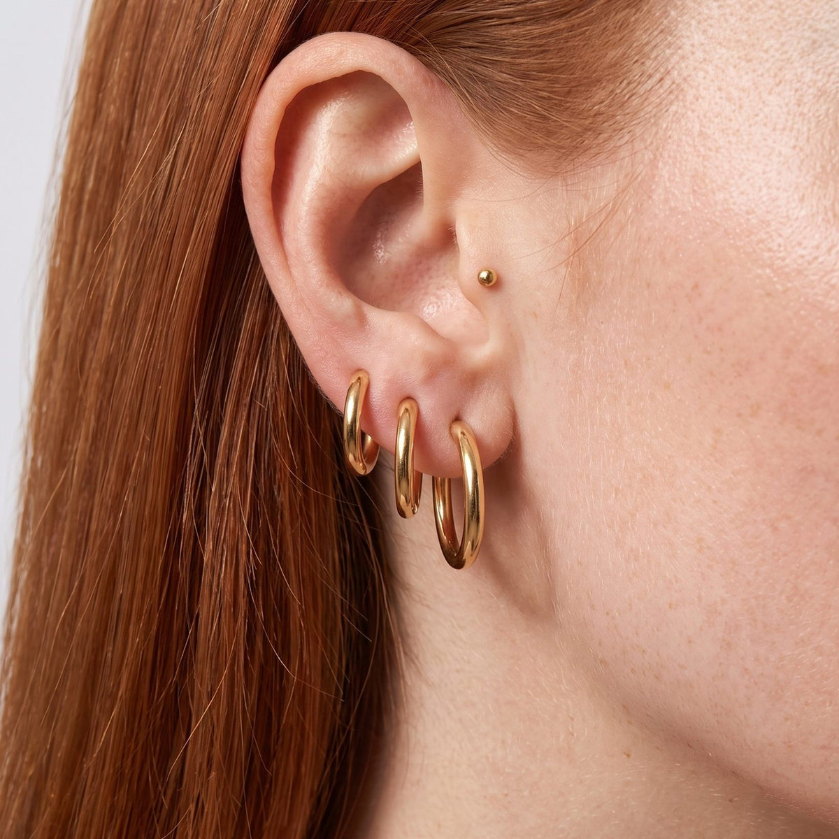 Woman wearing the Amelia Classic Round Hoops on her lobe in a polished gold color