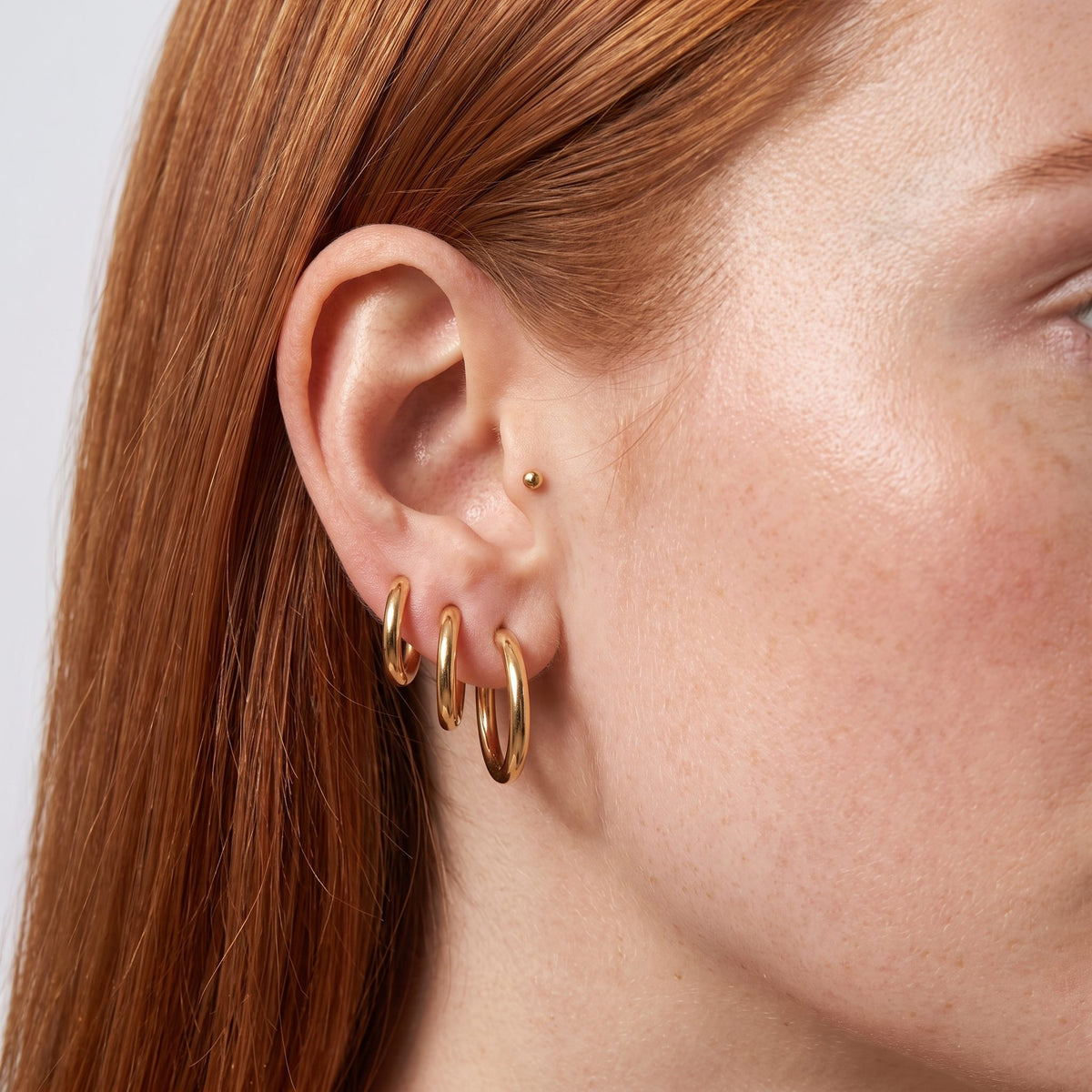 Woman wearing the Amelia Classic Round Hoops on her lobe in a polished gold color