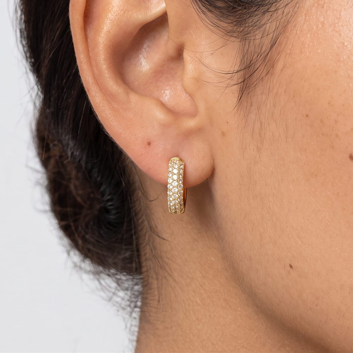 Woman wearing the Amélie Chunky Paved Huggies on the lobe, featuring a gold band paved with crystals