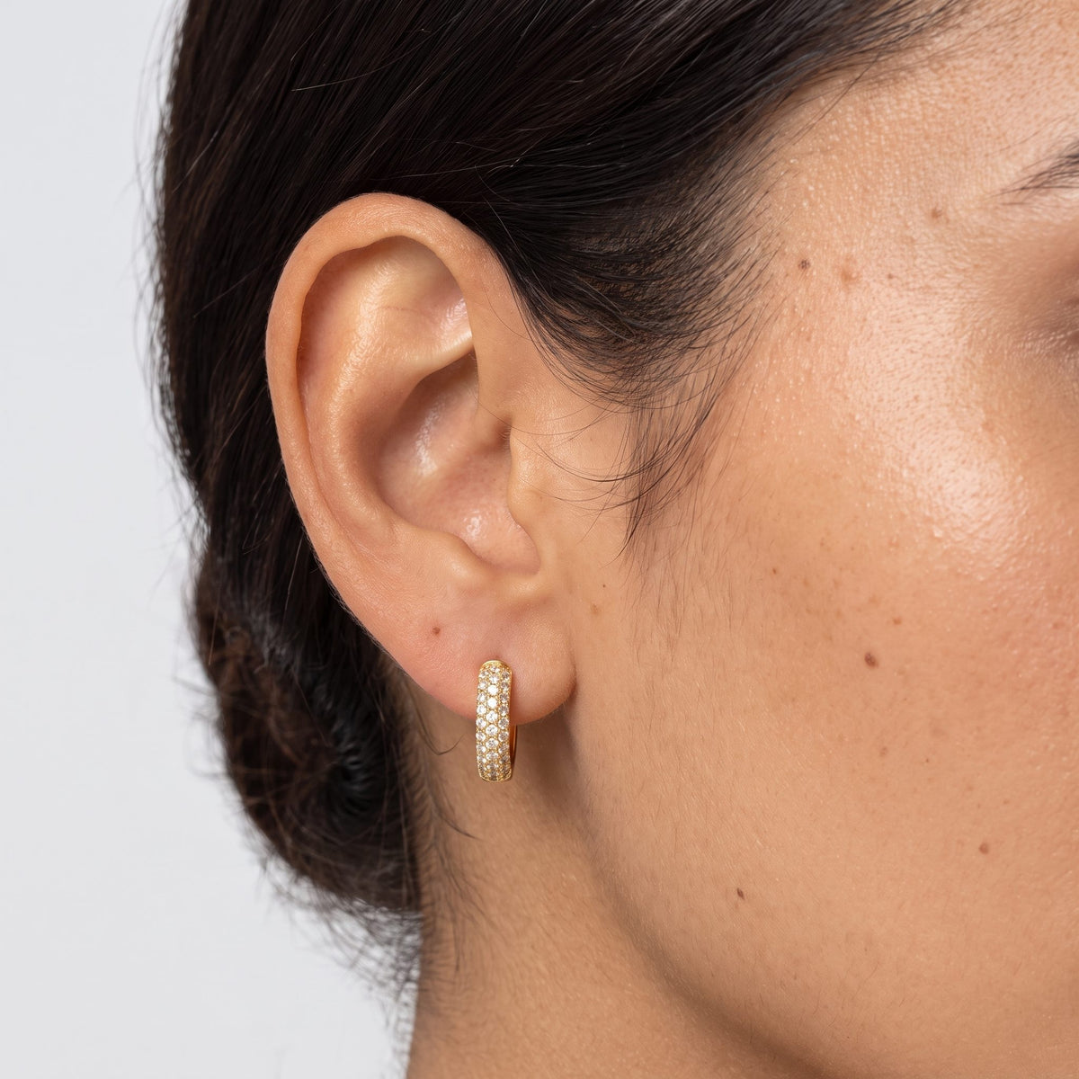 Woman wearing the Amélie Chunky Paved Huggies on the lobe, featuring a gold band paved with crystals