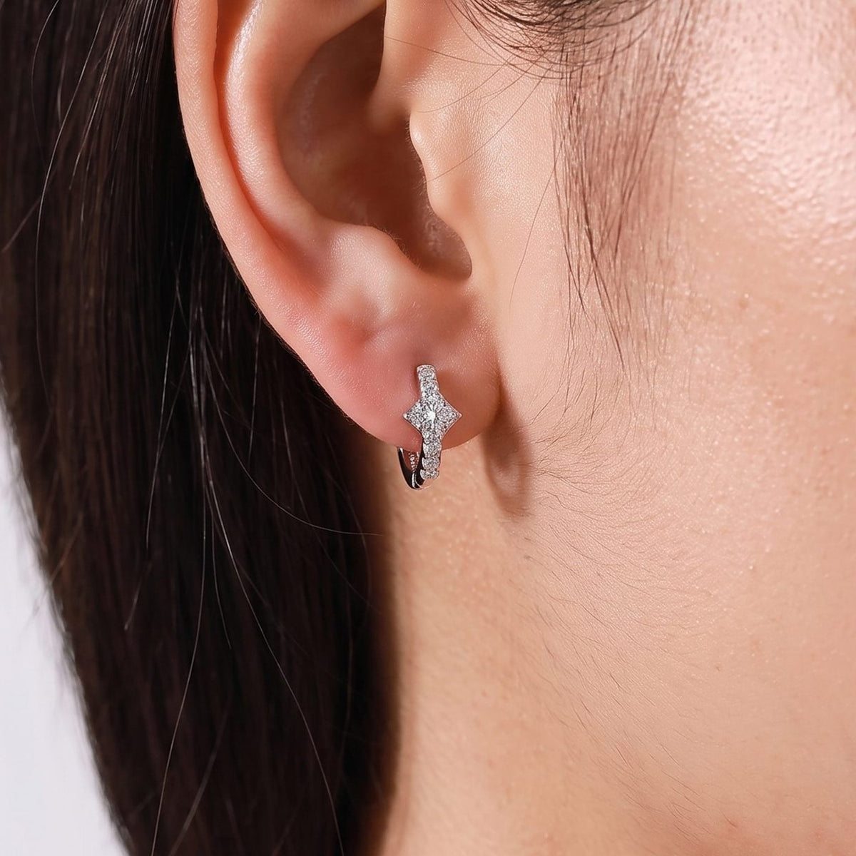 Woman wearing the Anais Crystal Glow Hoops on the lobe, featuring a silver four-point star design