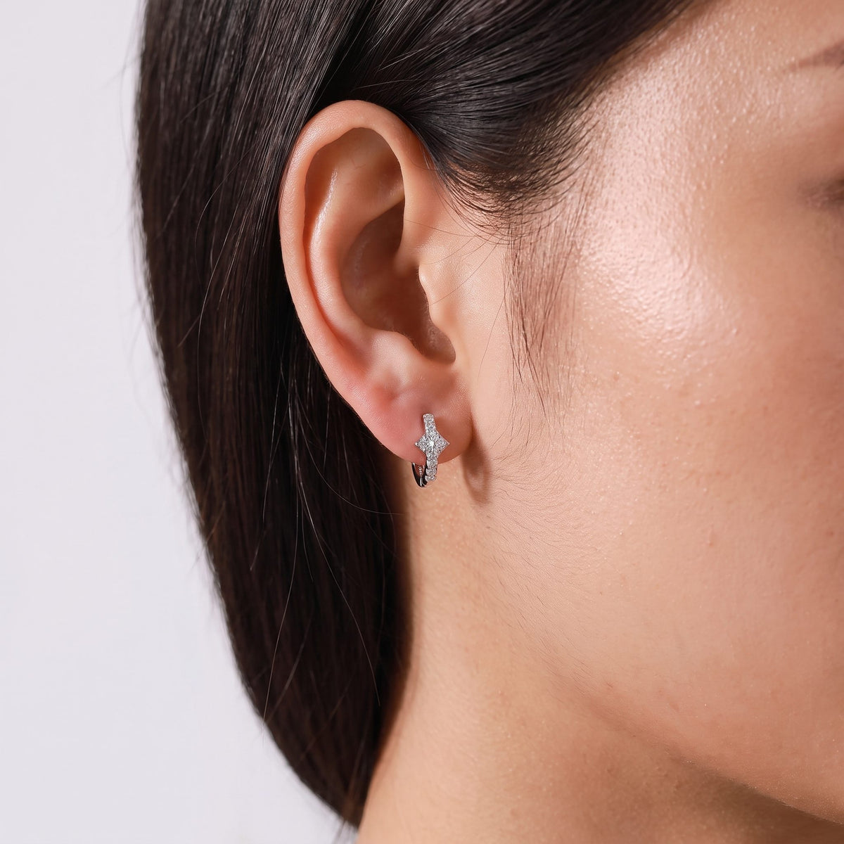 Woman wearing the Anais Crystal Glow Hoops on the lobe, featuring a silver four-point star design