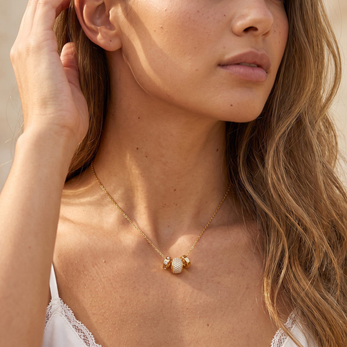 Woman wearing the Barrel Charm Necklace at the collarbone, with her hand touching her hair