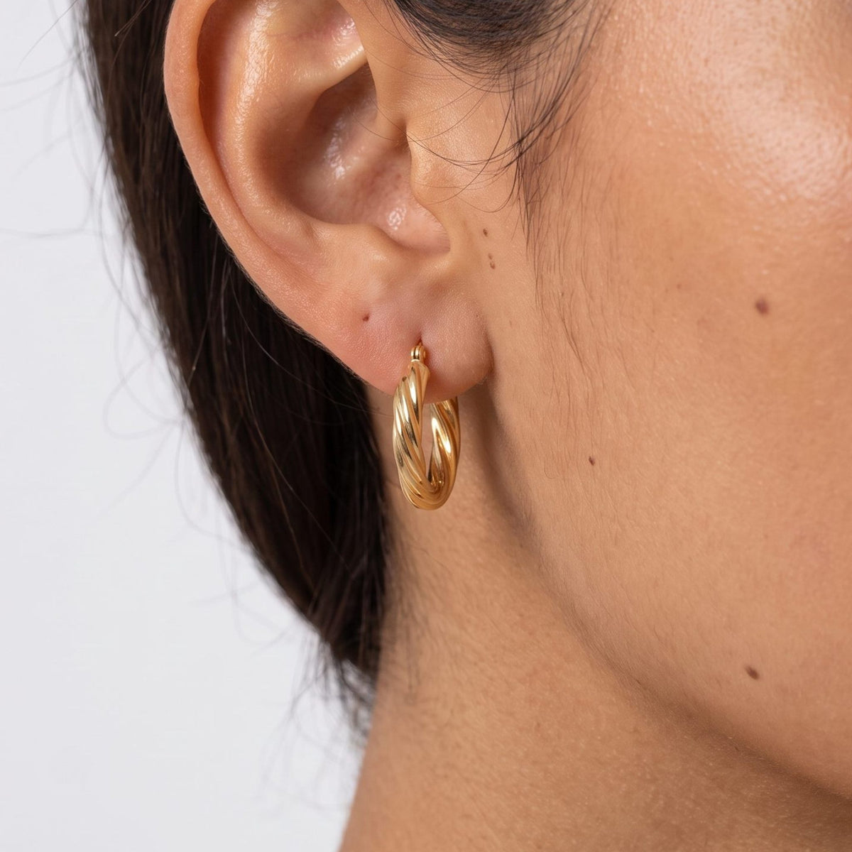 Close view of a woman wearing the Camila Twist Gold Hoops with a twisted design through the lobe