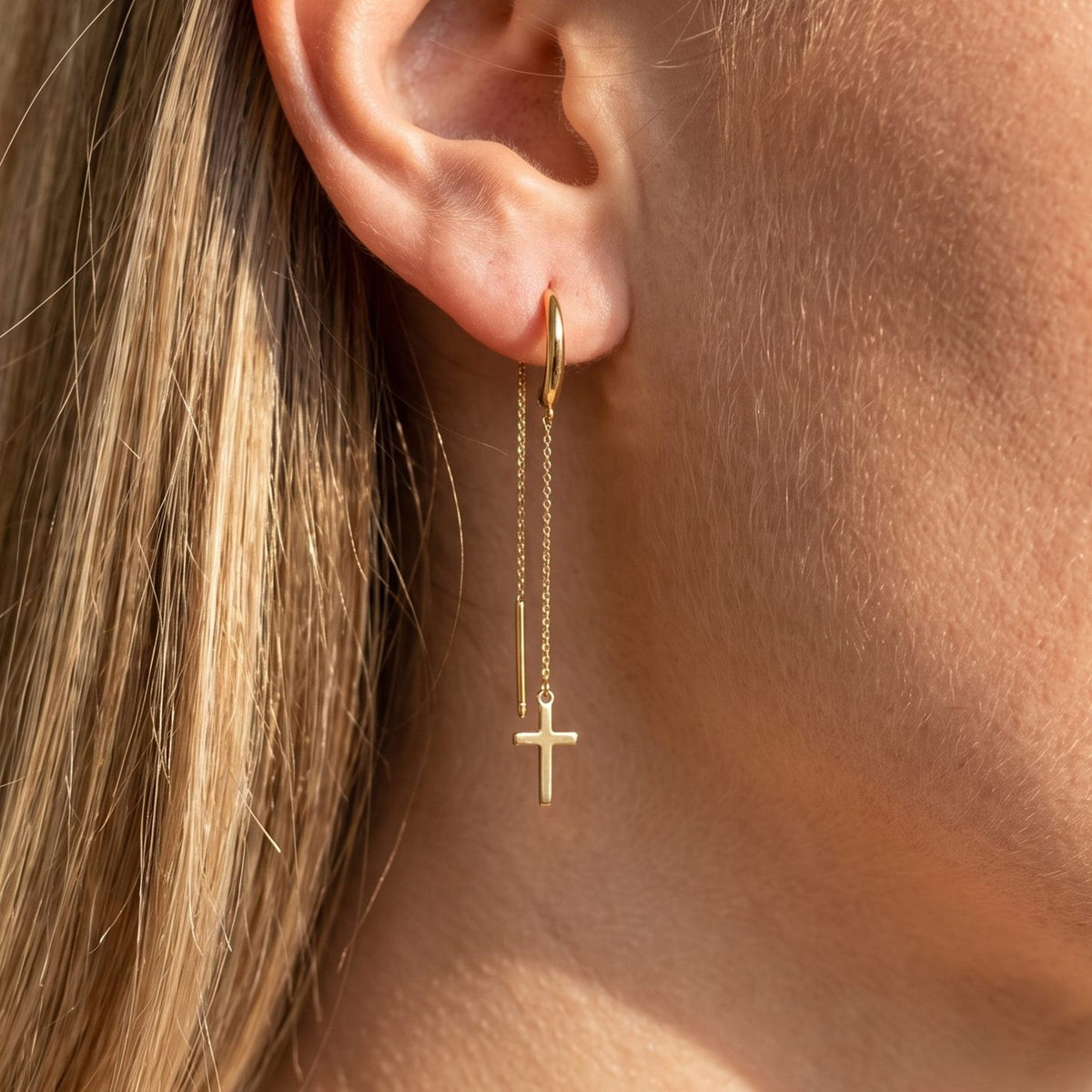Close view of a woman wearing the Camille Cross Chain Earrings on the lobe with a dangling gold cross