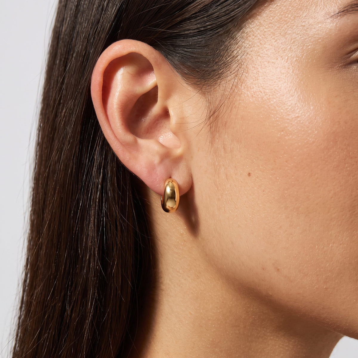 Close view of a woman wearing the Hailey Gold Earrings, a chunky smooth hoop through the lobe