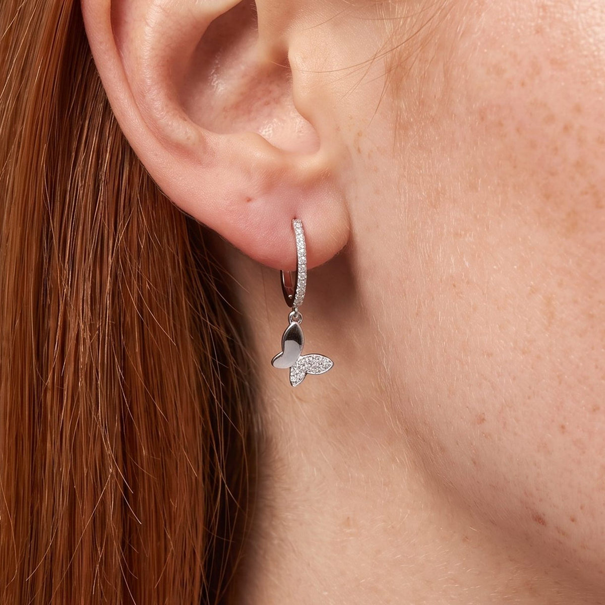 Woman wearing the Celina Butterfly Charm Earrings hanging below the lobe with a sparkling silver butterfly charm