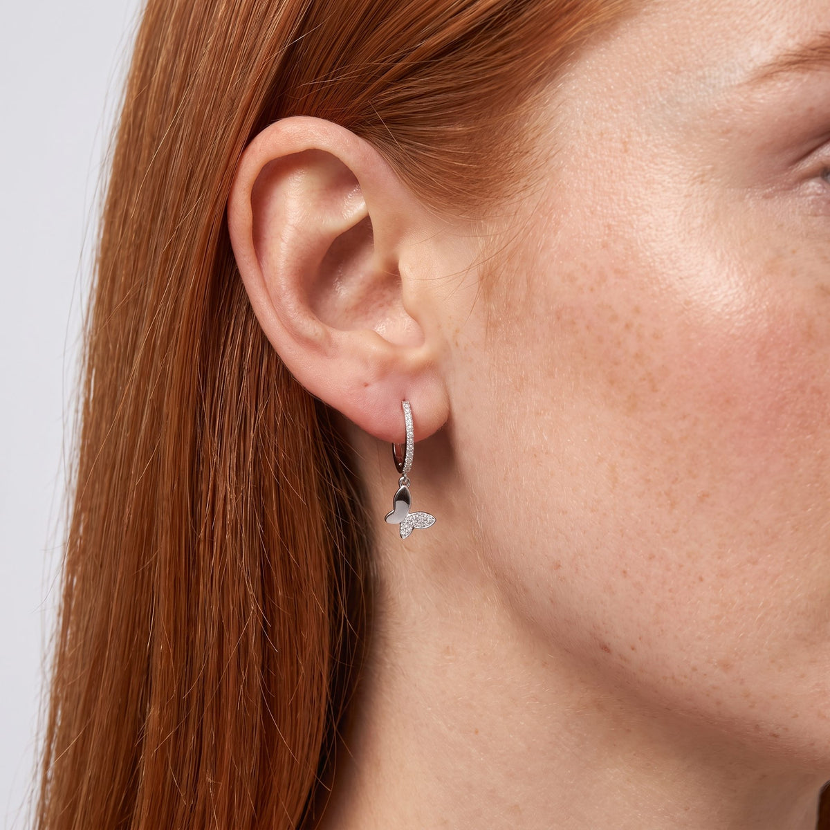 Woman wearing the Celina Butterfly Charm Earrings hanging below the lobe with a sparkling silver butterfly charm