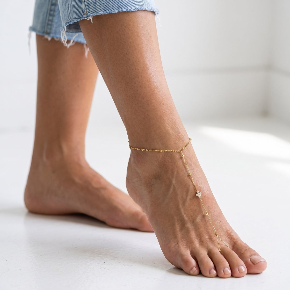 Wider view of a woman wearing the Clover Barefoot Anklet on her ankle