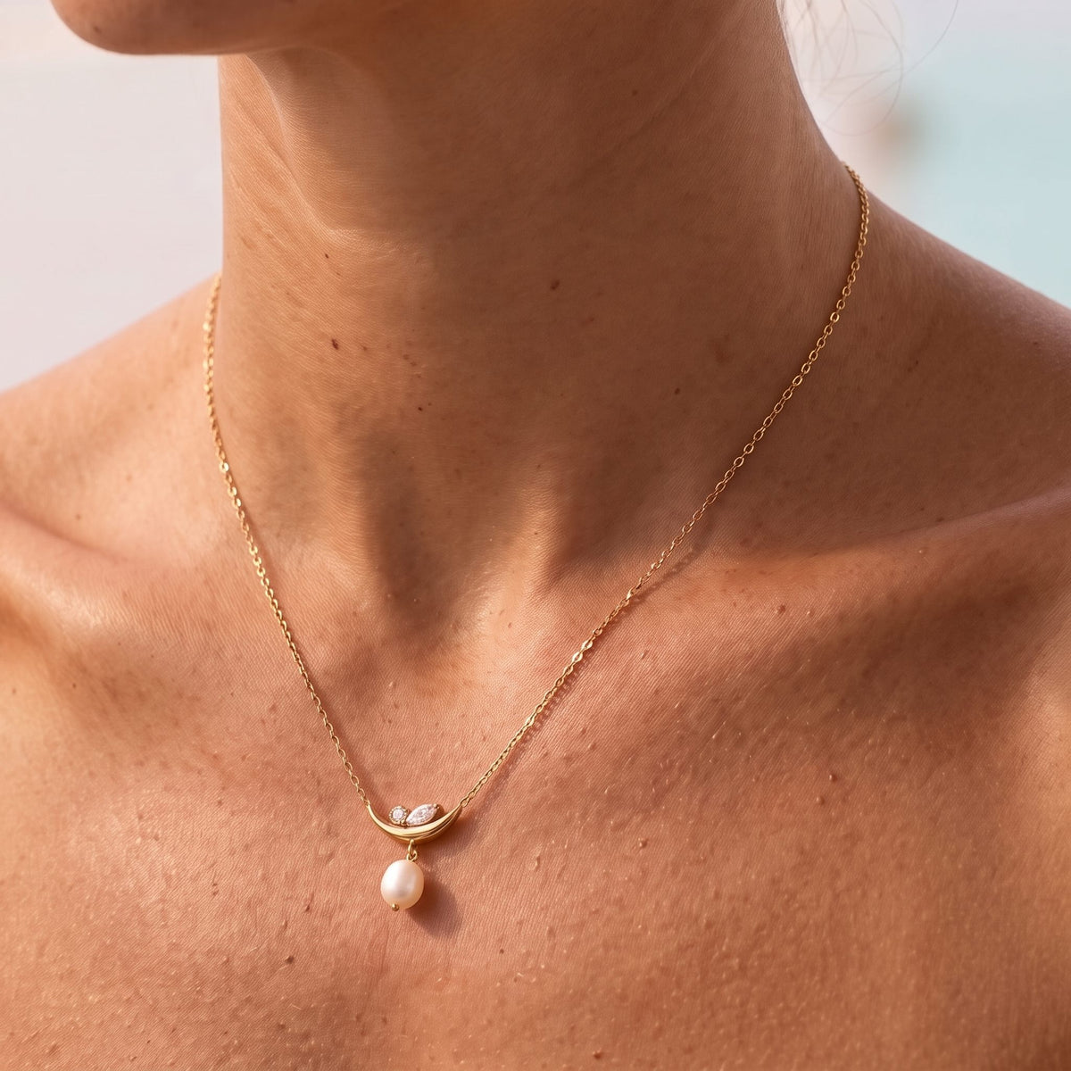 Close-up of the Crescent Pearl Pendant at the collarbone, showing its luminous pearl drop on warm skin, in rose gold