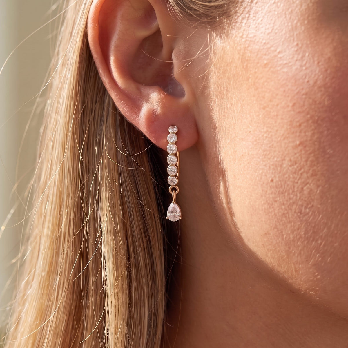 Close-up of the Crystal Drop Earrings on the ear, glowing in warm natural sunlight, in rose gold