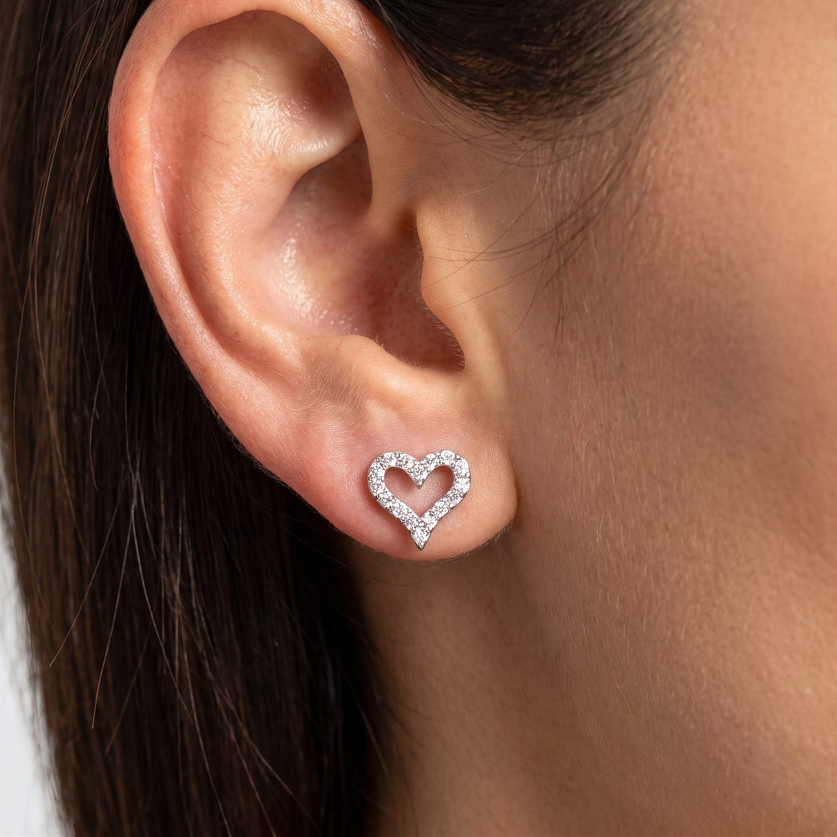 Woman wearing the Daniella Crystal Heart Earrings flat to the lobe, featuring a sparkling silver heart outline