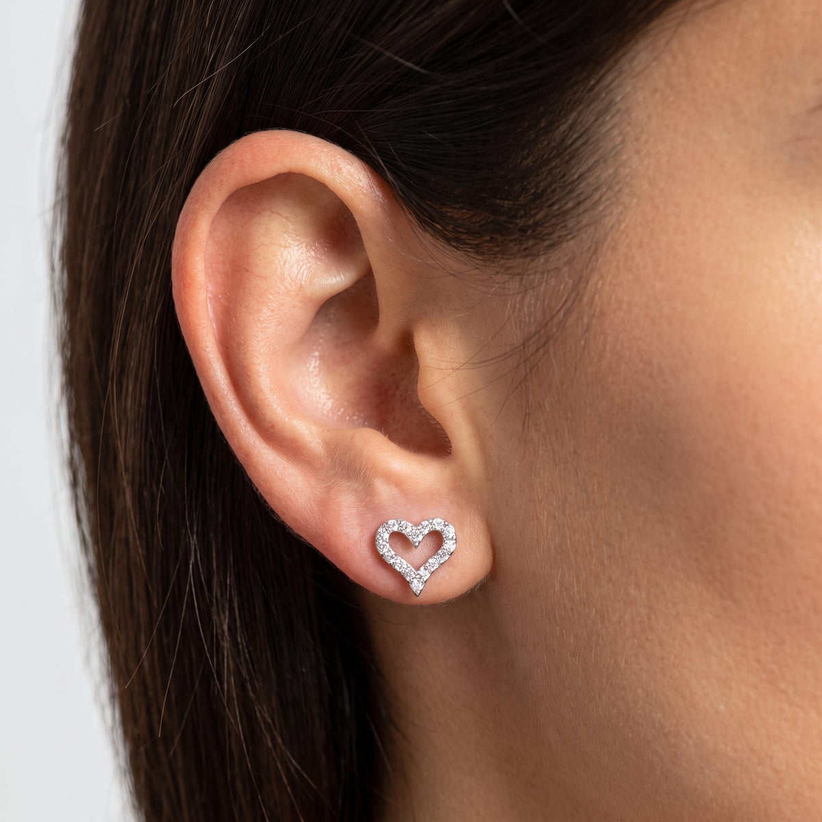 Woman wearing the Daniella Crystal Heart Earrings flat to the lobe, featuring a sparkling silver heart outline