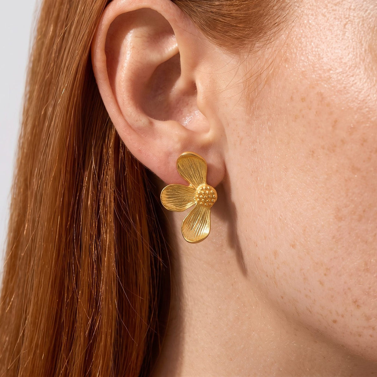 Close view of a woman wearing the Éden Petal Gold Earrings, a textured flower shape on her lobe