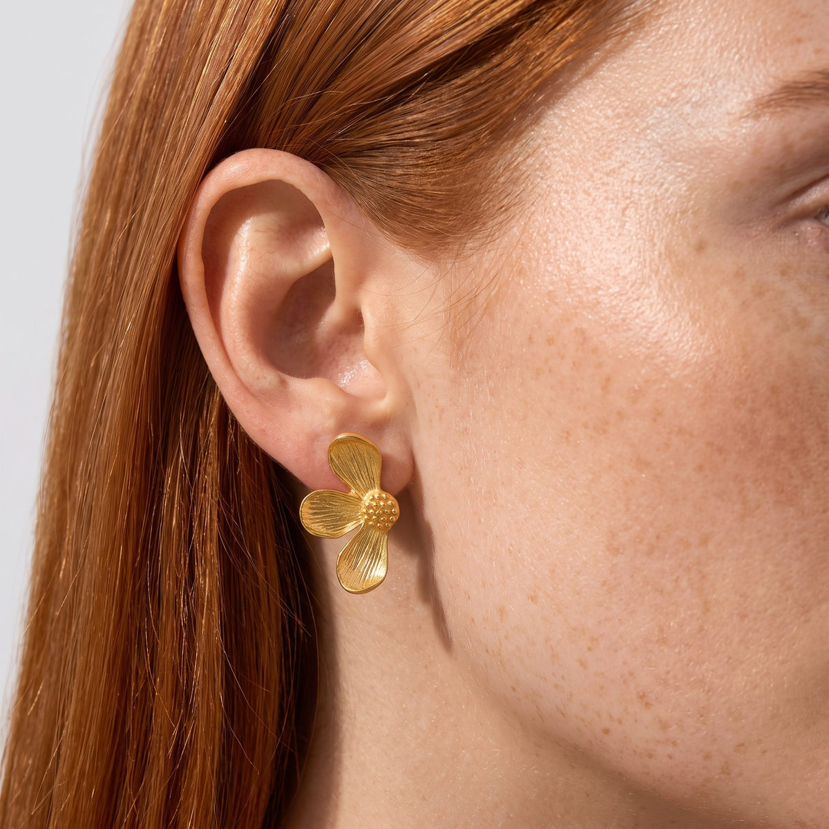 Close view of a woman wearing the Éden Petal Gold Earrings, a textured flower shape on her lobe