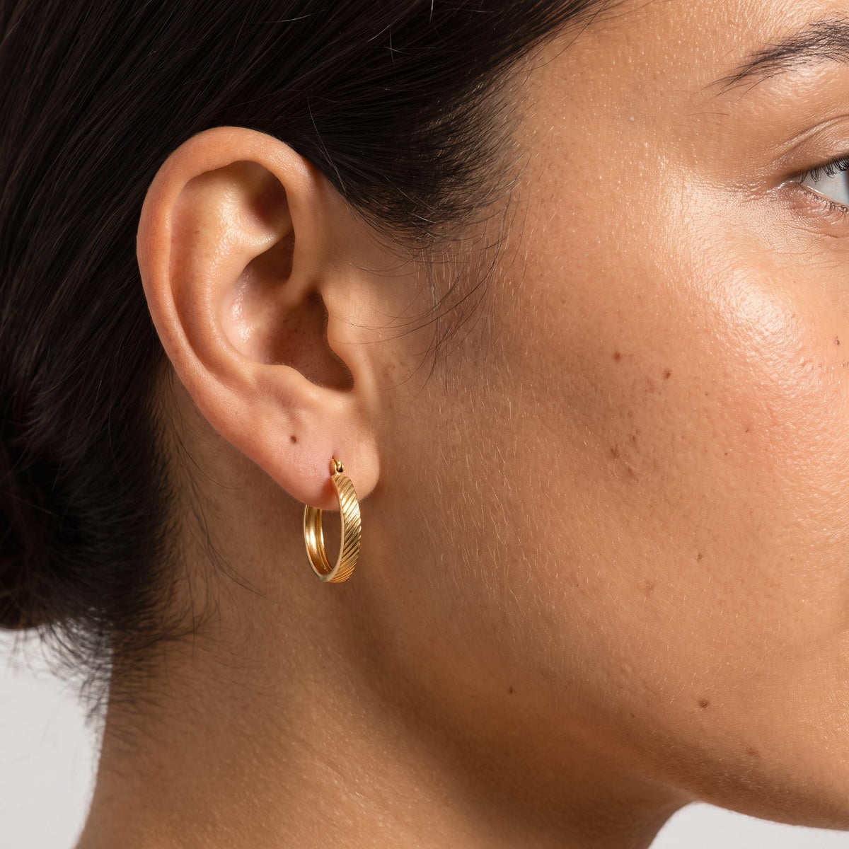 Woman wearing the Elanor Gold Hoop Earrings through the lobe, featuring a textured ribbed pattern