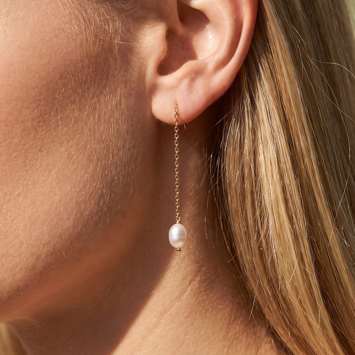 Woman wearing the Élise Dainty Pearl Earrings hanging below the lobe on a delicate gold chain