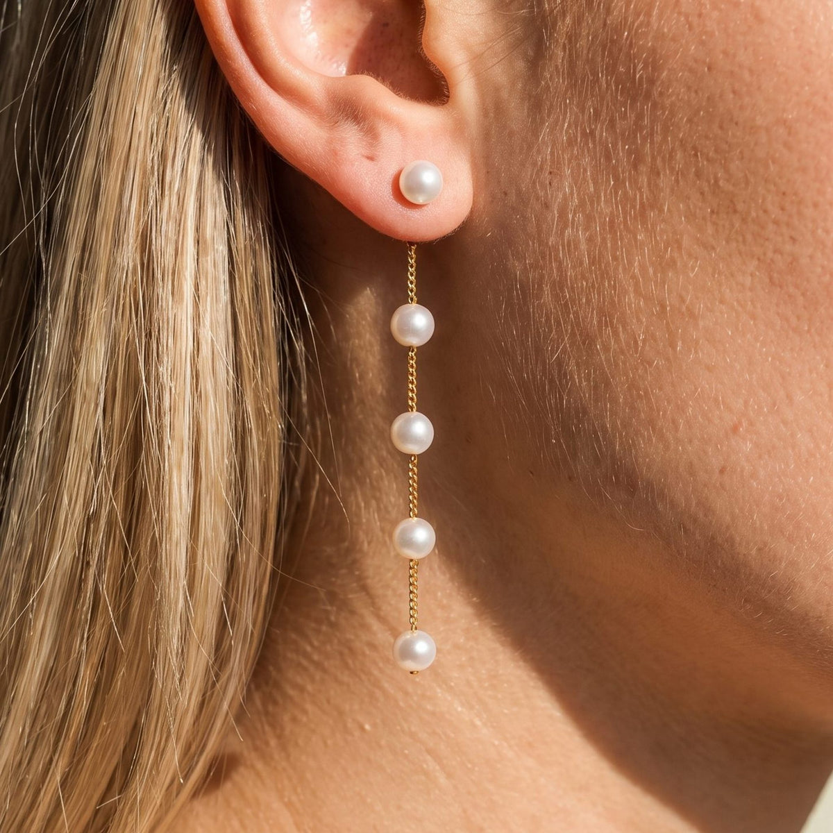 Woman wearing the Élise Drop Pearl Earrings hanging below the lobe with a gold chain of spaced pearls