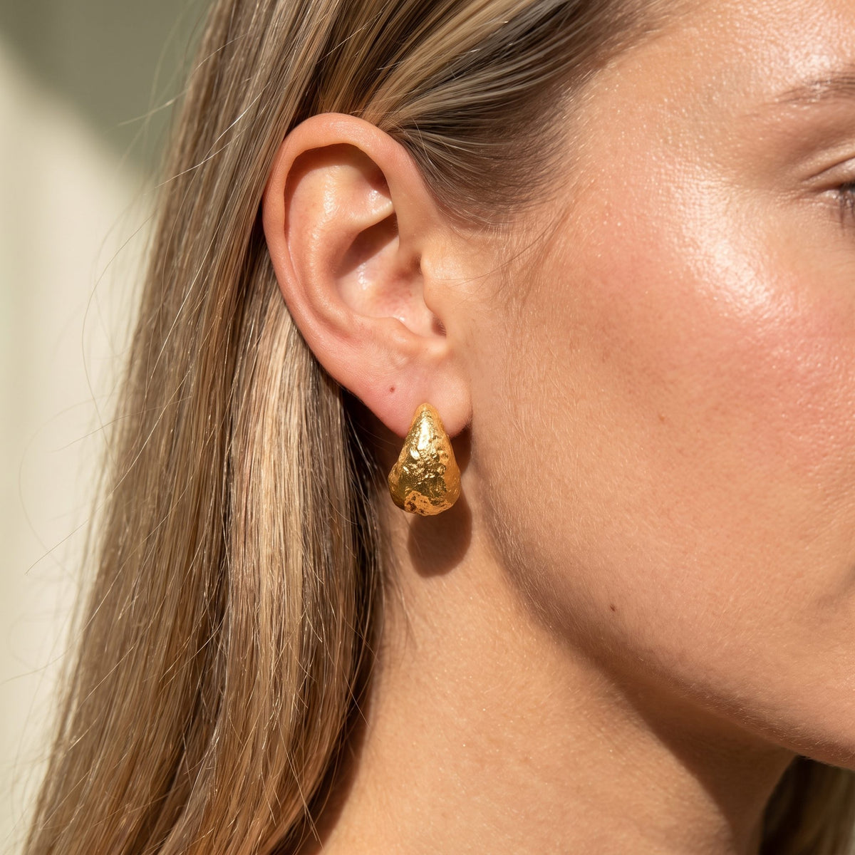 Woman wearing the Élise Sculpted Drop Gold Earrings hanging below the lobe with a textured finish