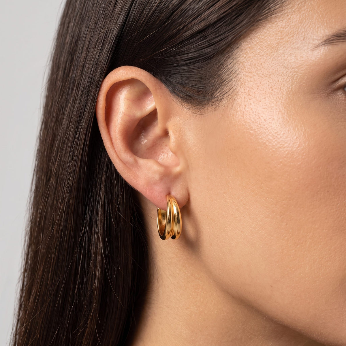 Close view of a woman wearing the Emily Wave Earrings, a gold double hoop through the lobe
