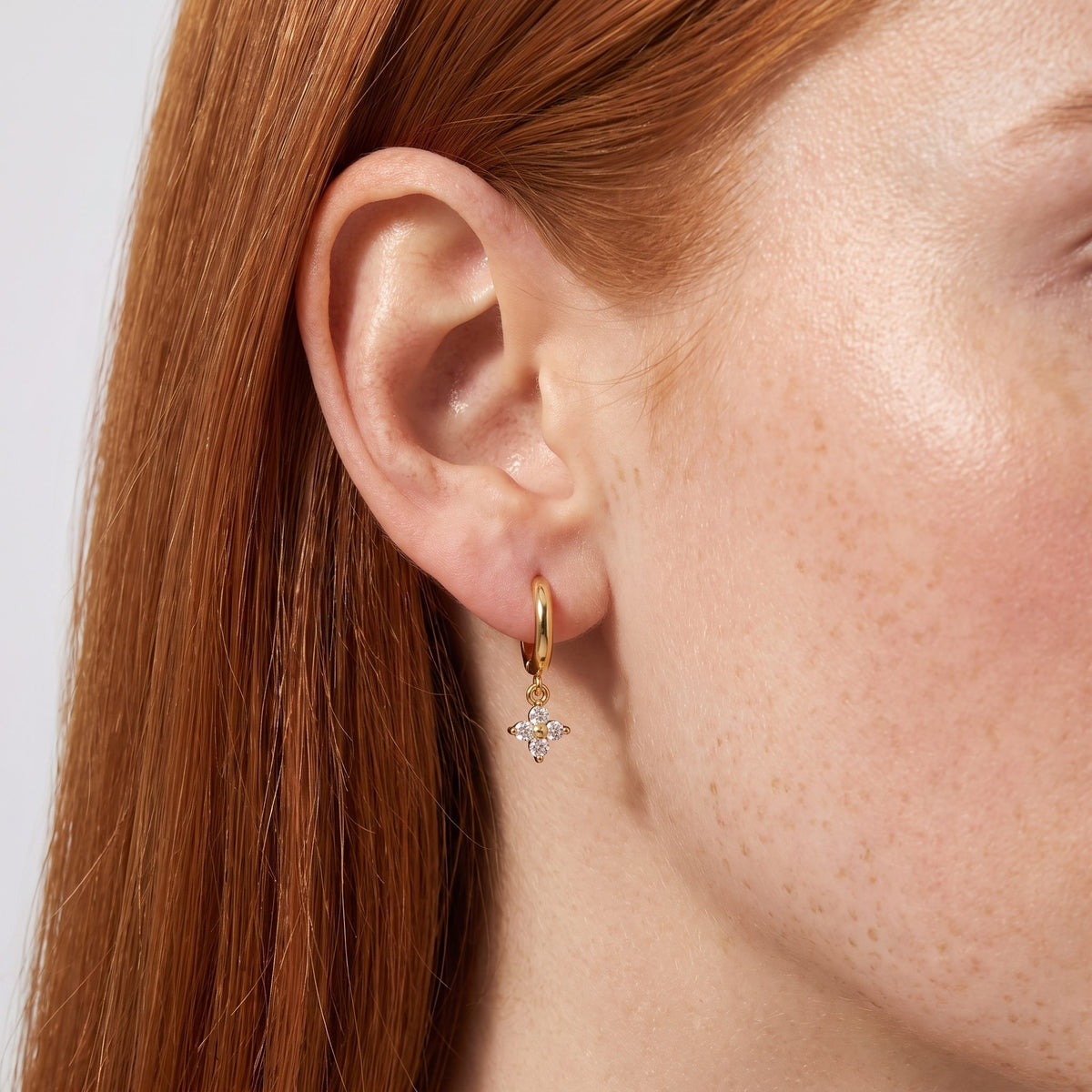 Woman wearing the Emma Crystal Clover Earrings hanging below the lobe on a small gold hoop
