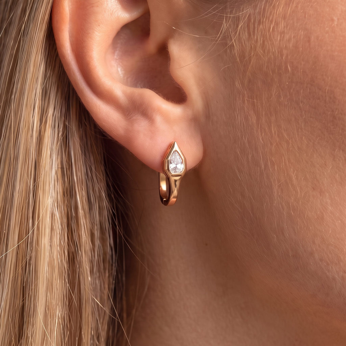Close-up of the Geometric Pear Huggies on an earlobe highlighting the pear-cut crystal setting, in rose gold