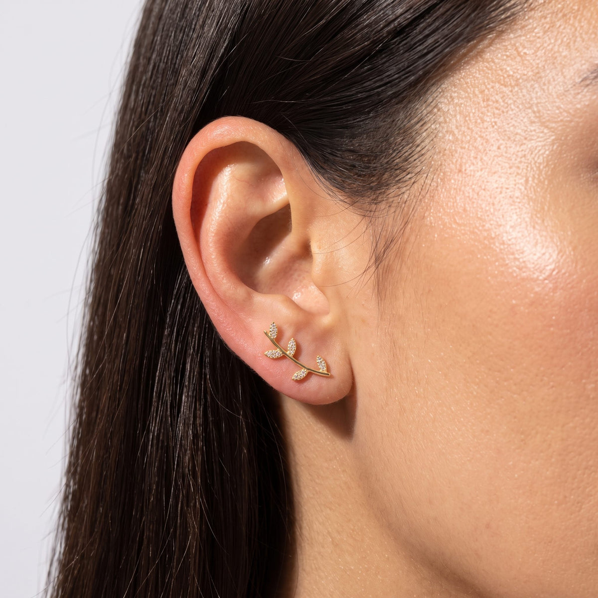 Woman wearing the Giulia Vine Leaf Earrings on the lobe, featuring a curved gold branch with stones