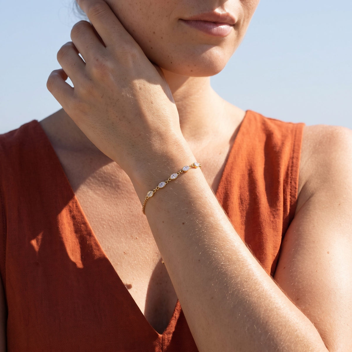 Woman wearing the Gold Oval Bezel Bracelet on the wrist, her hand raised near her neck