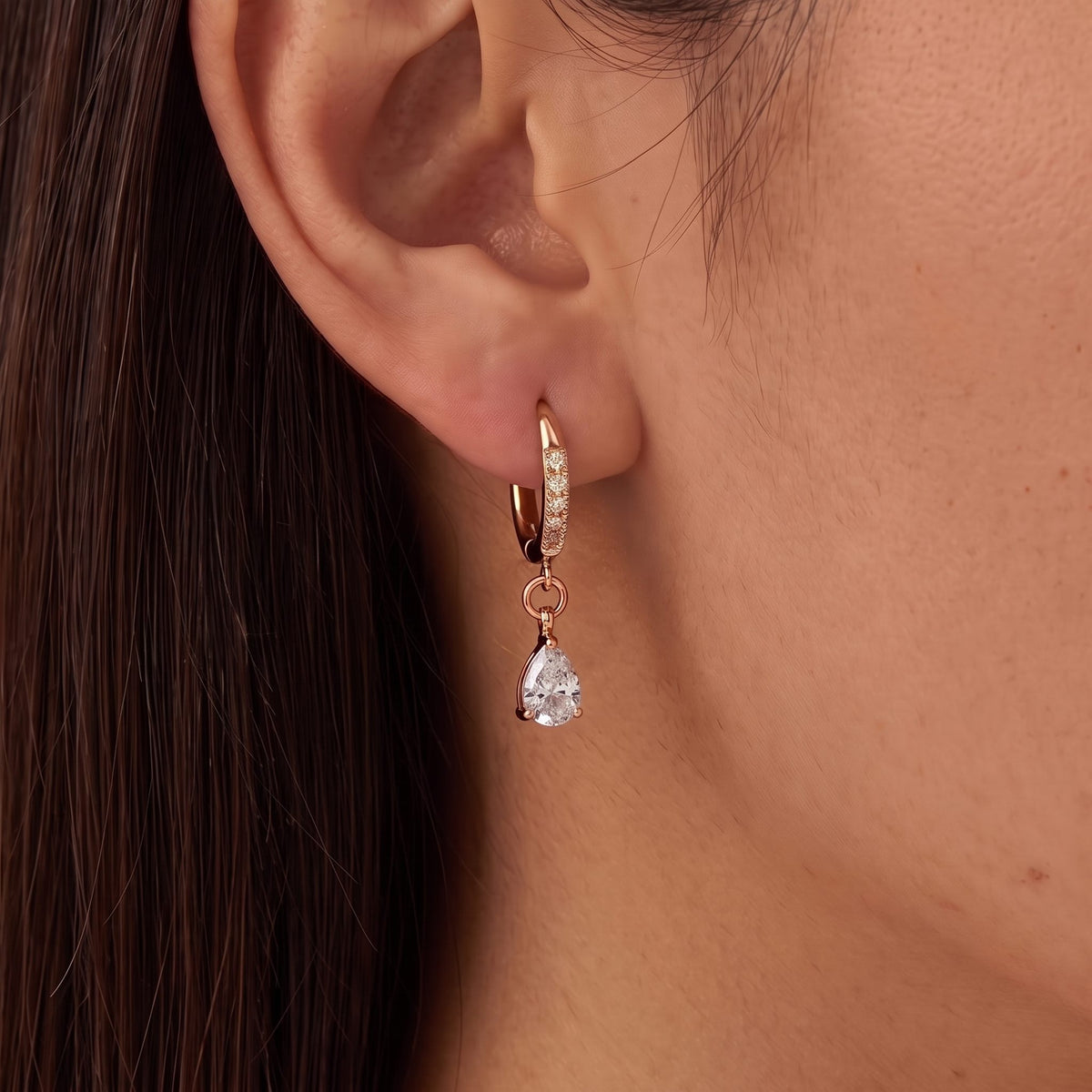 Woman with dark hair wearing the Pear Huggies in rose gold, a pear crystal hanging below the lobe