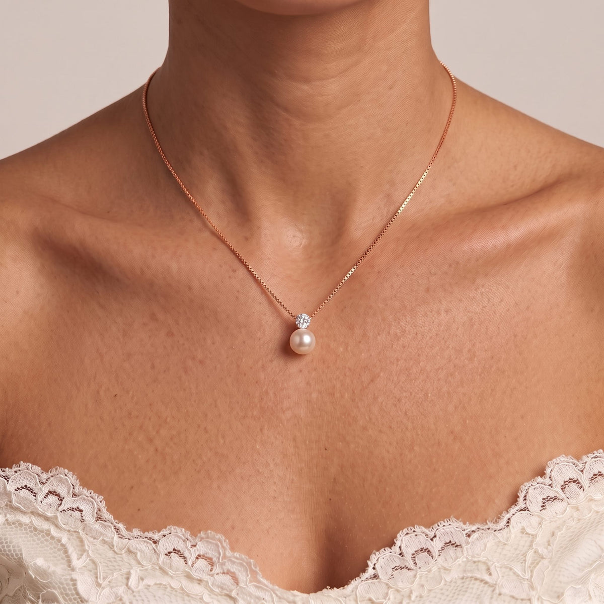 Close-up of the Pearl Pendant in rose gold on a fine chain at the collarbone, above a lace top