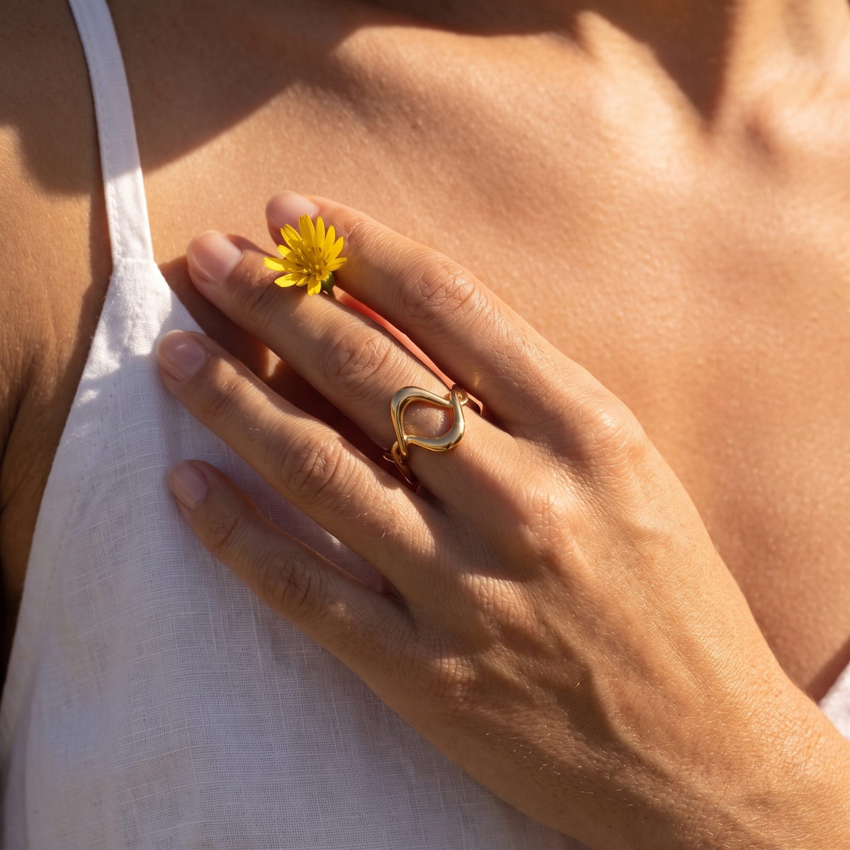 Woman wearing the Gold Twisted Wave Ring on her ring finger, holding a small yellow flower
