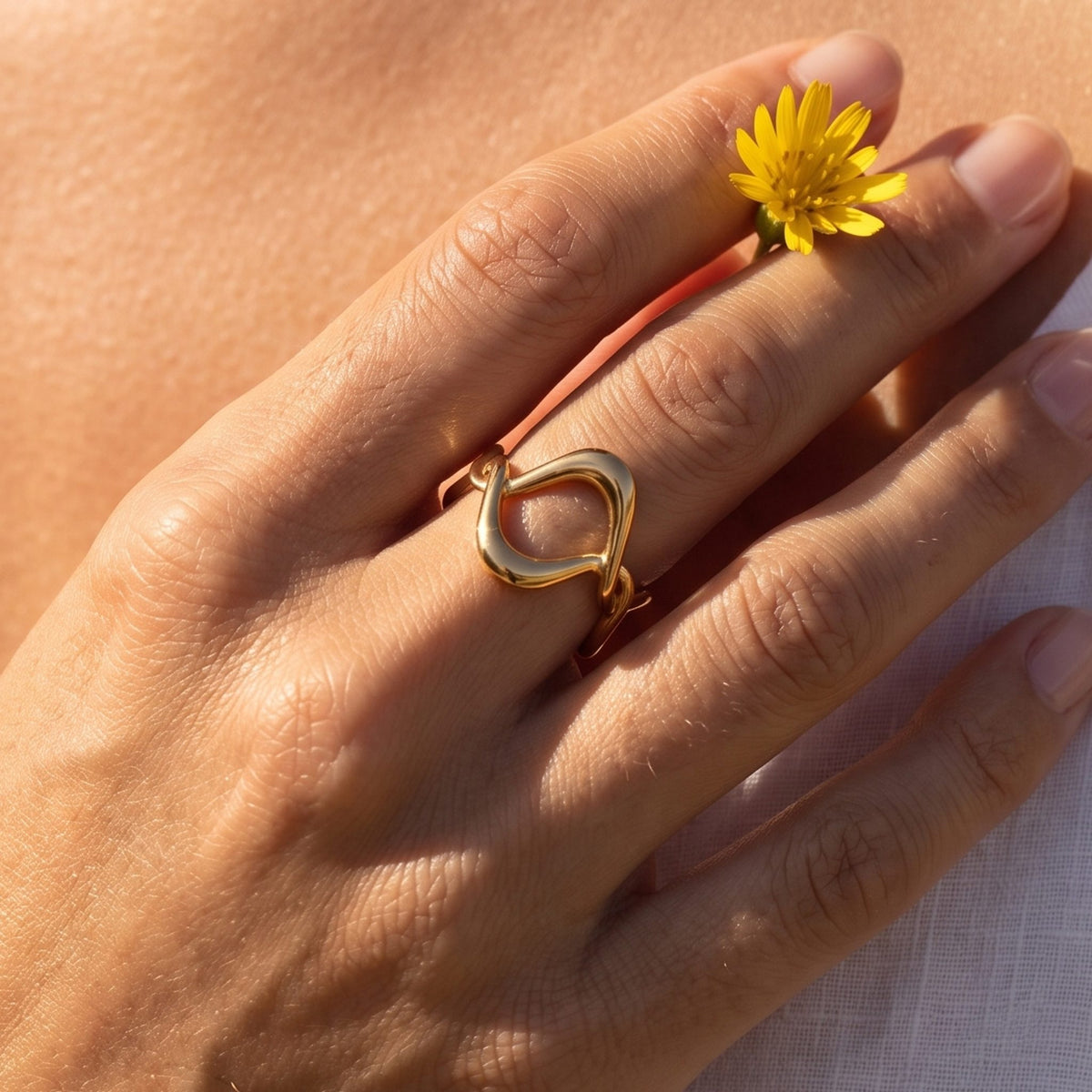Close-up of the Gold Twisted Wave Ring on a ring finger in warm natural light