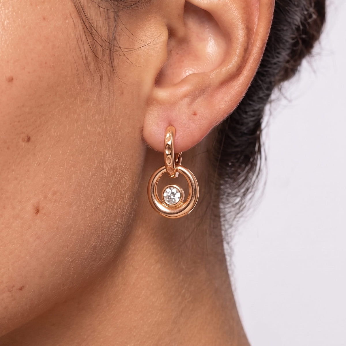 Close-up of the Hammered Circle Huggies on the ear showing the bezel-set crystal detail, in rose gold