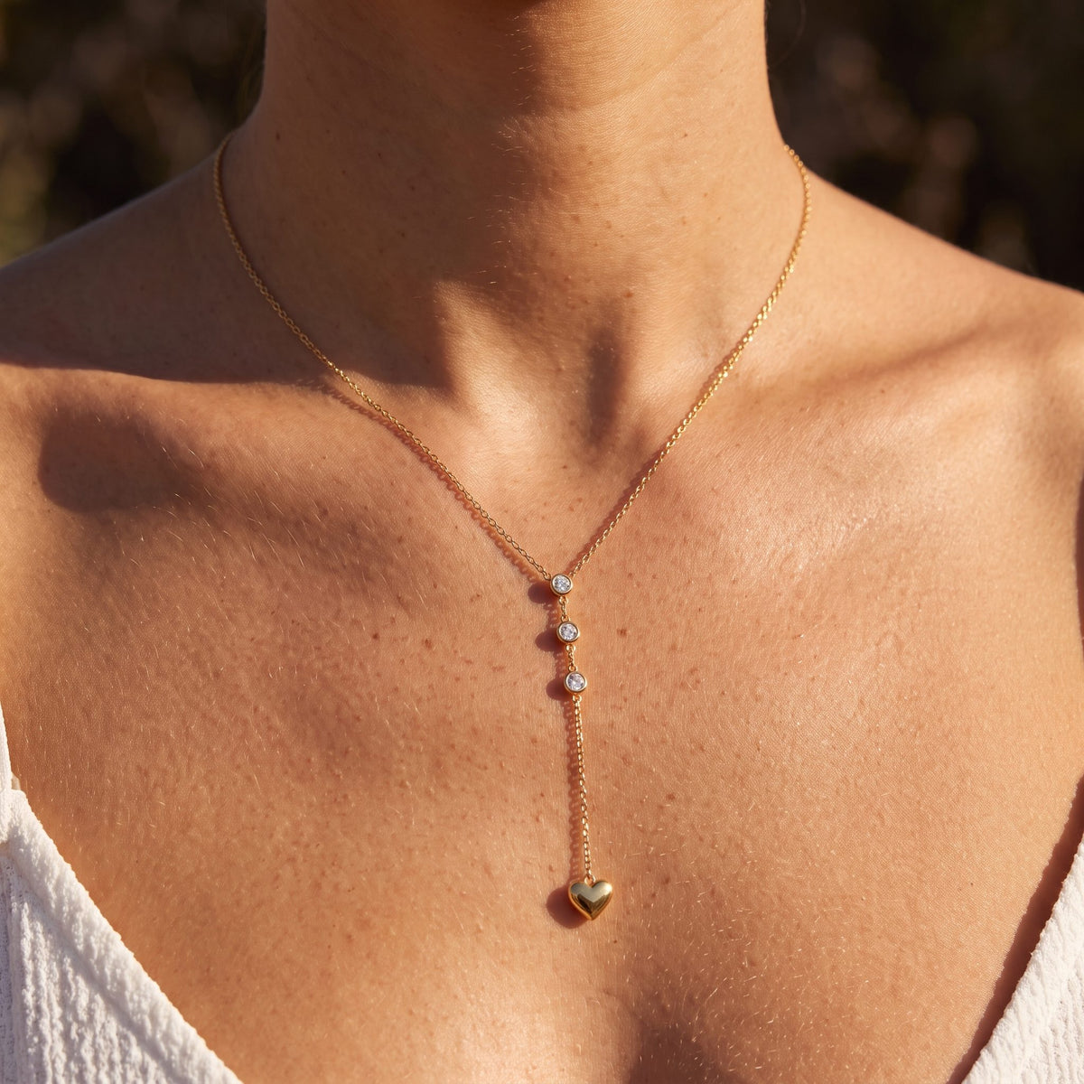 Woman wearing the Heart Lariat Necklace at the collarbone illuminated by warm sunlight