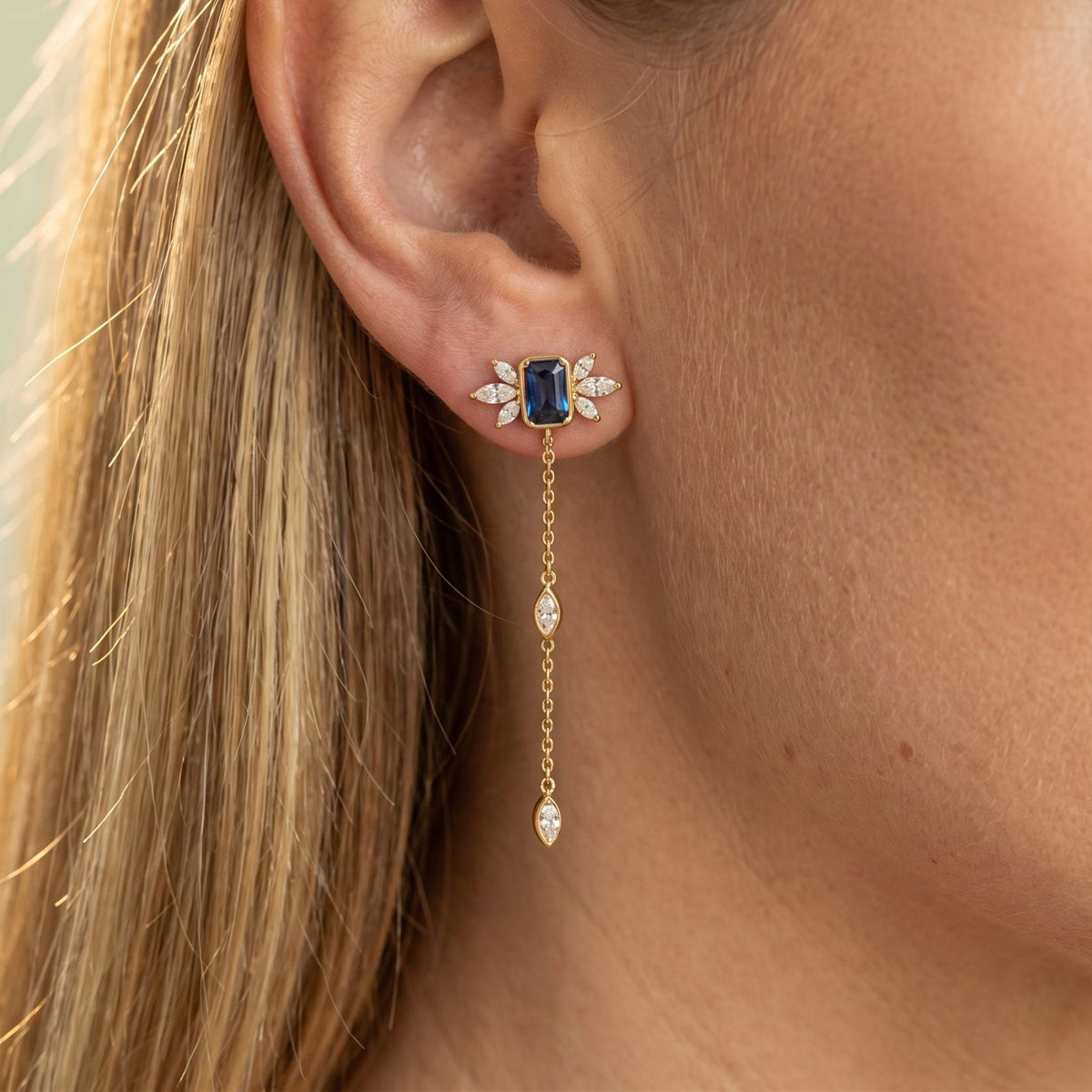 Woman wearing the Isabella Noir Drop Earrings on the lobe with a blue stone and hanging gold chain