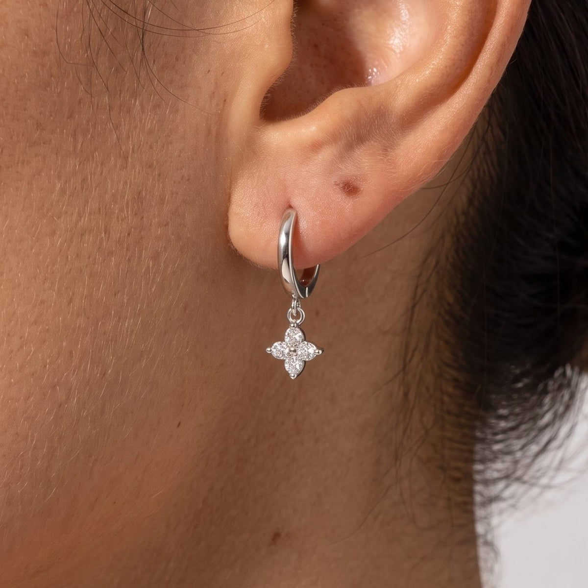 Woman wearing the Juliette Clover Crystal Hoops through the lobe with a silver clover charm hanging below