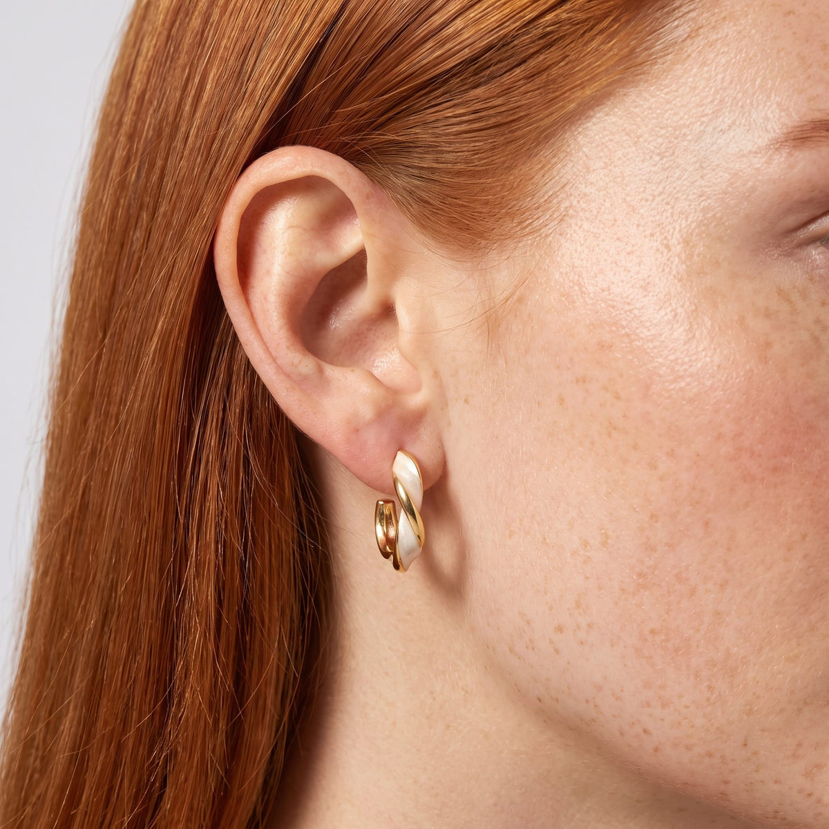 Woman wearing the Lacey Twist Hoop Earrings hanging below the lobe with a gold and white twisted design
